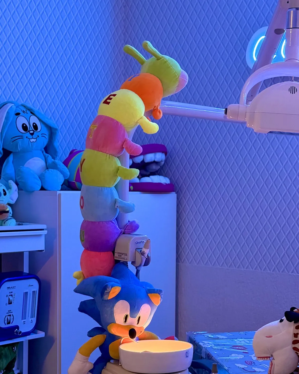 Lagarta de pelúcia colorida e brinquedos no consultório, sob luz azul